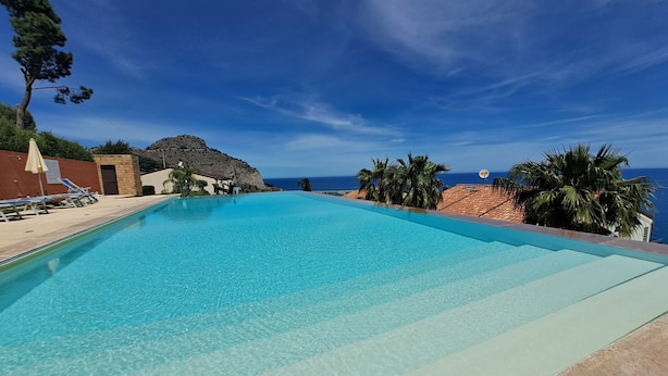 Une piscine d’un bleu éclatant, dotée de chaises longues, un mur de pierre et une vue sur l’océan.