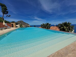 Una piscina azul cristalina con sillones de descanso, un muro de piedra y vista al océano.