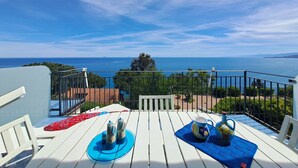 Un balcon avec une table blanche, deux salières et poivrières, un set de table bleu et un pichet orné de motifs floraux.