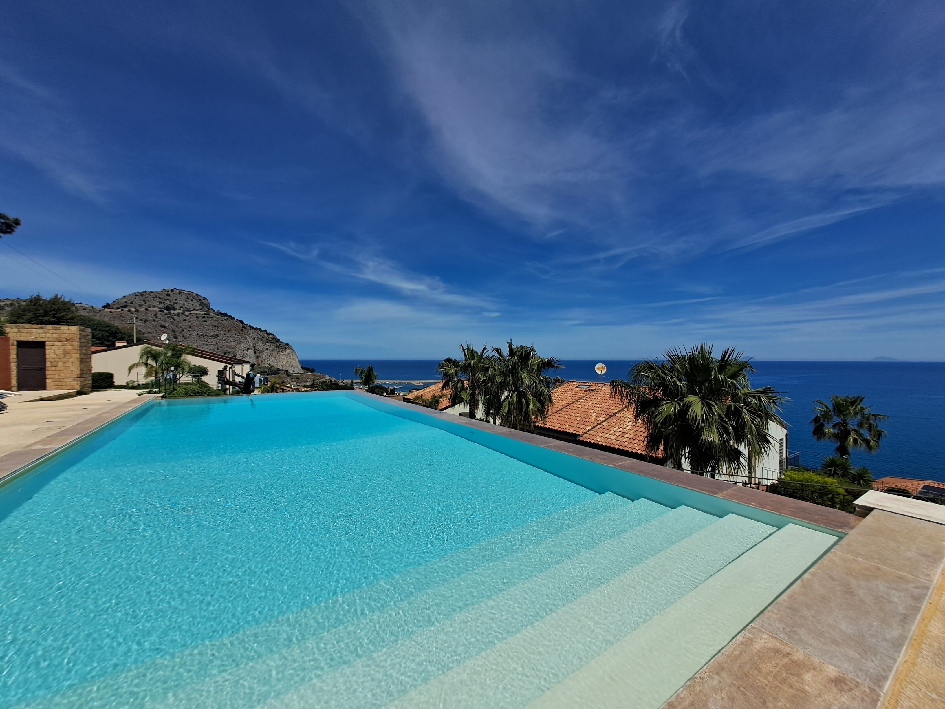 A clear blue swimming pool with a view of the ocean and a mountain in the background.