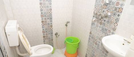 A small bathroom with a toilet, a green bucket, a shower, and a sink.