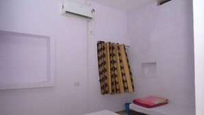 A small, clean room with a single bed, a window with a curtain, and an air conditioning unit on the wall. - Maharani Maya Guest House Bodhgaya  (Gaya)