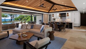 Amplia sala de estar con un sofá grande, una mesa de centro y una mesa de comedor. Cuenta con una cocina con armarios blancos y vistas al exterior.
