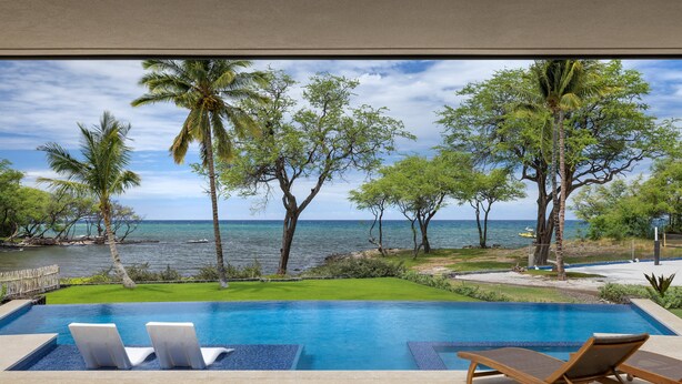 Una piscina con sillas de descanso, vistas al océano y palmeras.