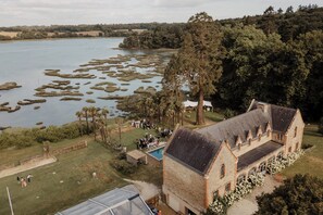 Un grand bâtiment historique doté d’une piscine et d’une pelouse, entouré d’arbres et bordé d’un lac.