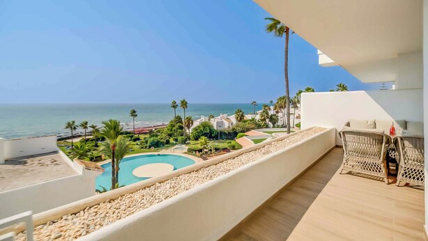 Un balcón con vista a una piscina, palmeras y una playa.