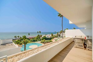 Un balcón con vista a una piscina, palmeras y una playa.