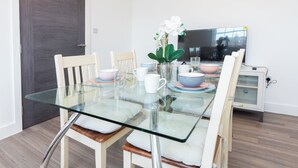A dining area with a glass table, white chairs, and a TV in the background. - Entire Reading Flat RG1 (Reading)