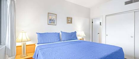 Una habitación de hotel con una cama grande, dos lámparas de noche, una puerta y dos cuadros en la pared.