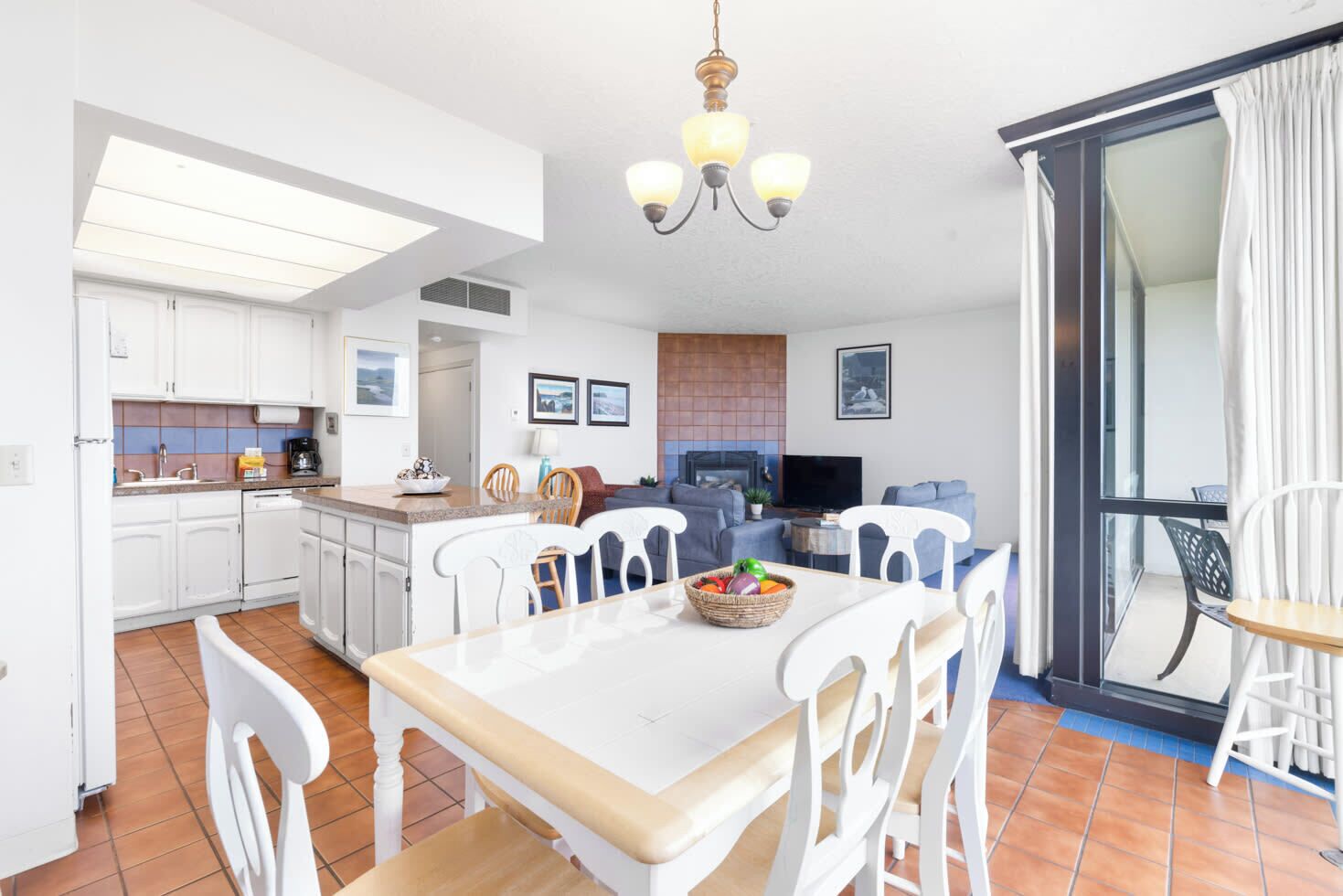 A modern kitchen with white cabinets, a dining table with chairs, a TV, and a fireplace.