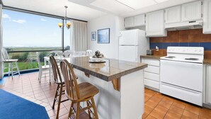 Une cuisine moderne dotée d’un grand îlot central, de meubles blancs et offrant une vue sur l’extérieur.