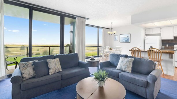 Un salon moderne avec deux canapés gris, une table basse ronde et une vue sur la campagne, visible à travers de grandes fenêtres.
