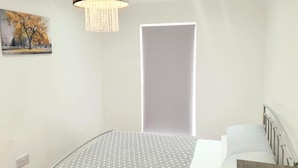 Un dormitorio con cama, lámpara colgante, un cuadro en la pared y una puerta.