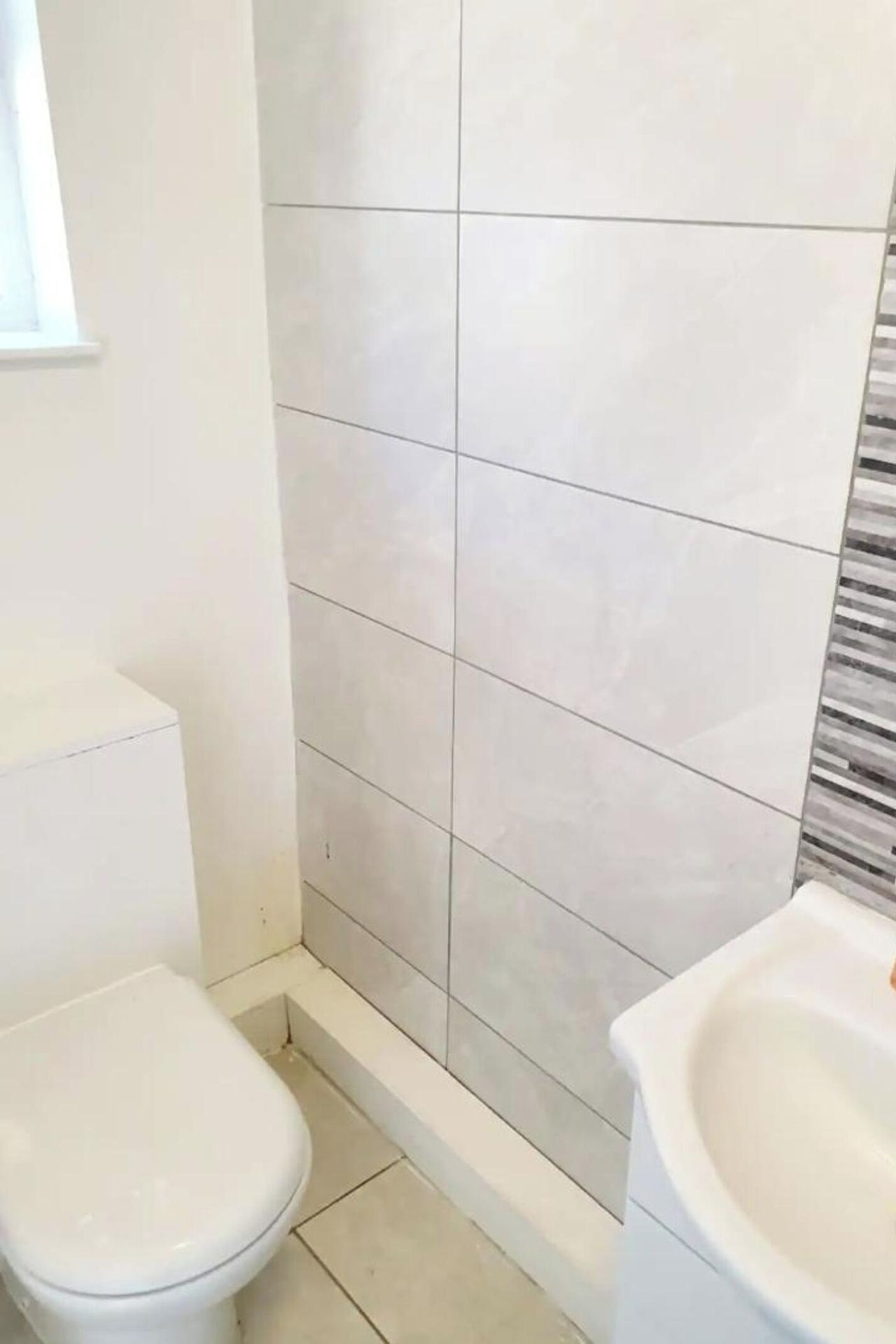 A bathroom with white tiles, a toilet, and a sink.