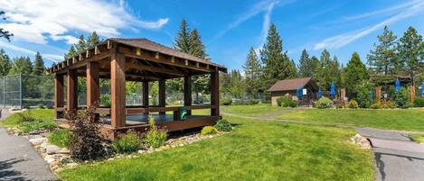 A wooden gazebo with a bench, surrounded by a well-maintained lawn and a clear sky.