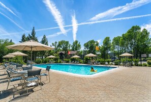 Une piscine entourée d’arbres, avec des chaises longues et des parasols, sous un ciel dégagé.