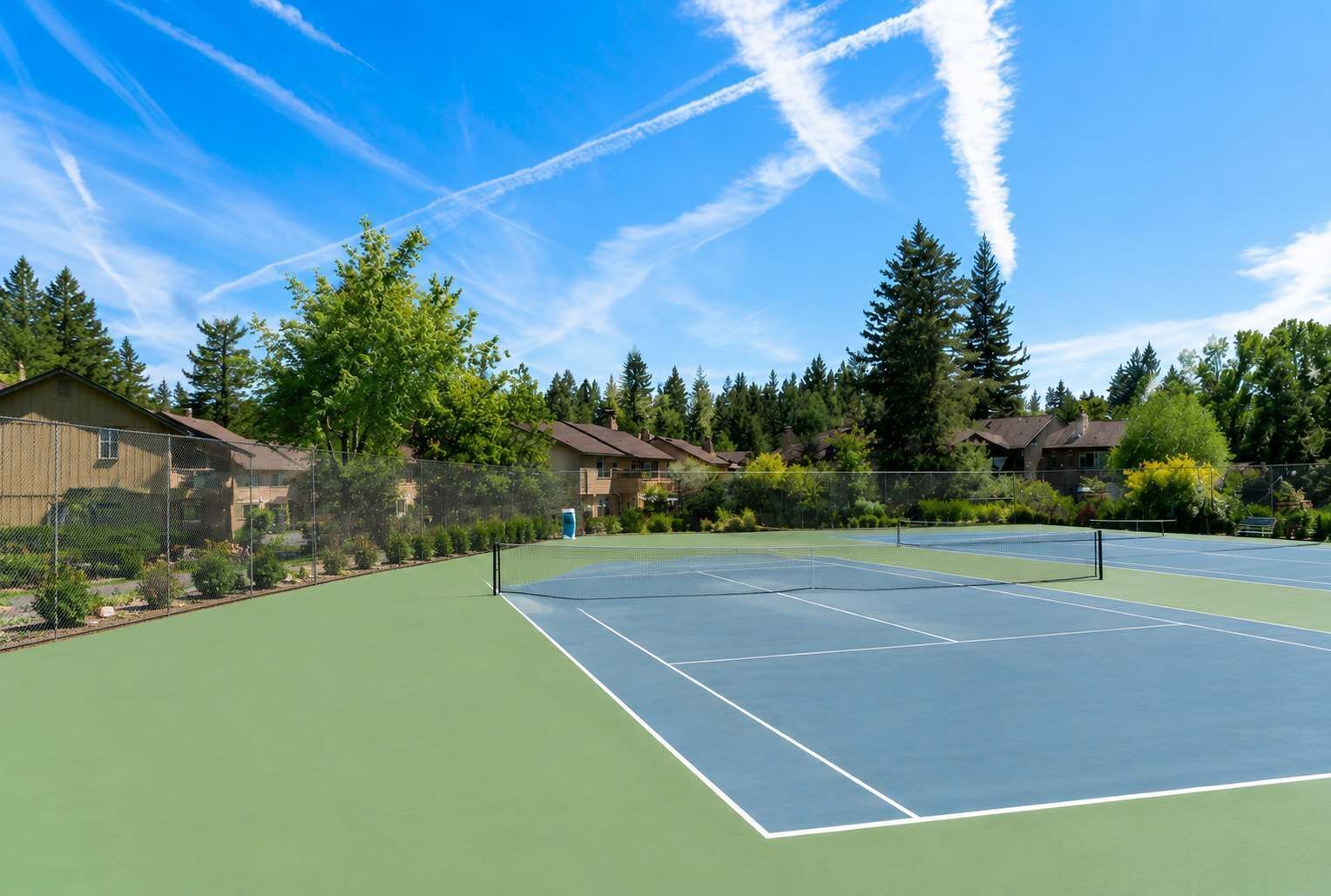 A tennis court with a net, surrounded by houses and trees.