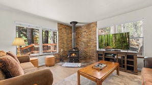A cozy living room with a stone fireplace, a large window with a forest view, and a comfortable seating area. - Tahoe Donner 4 bd Family Cabin (Truckee)