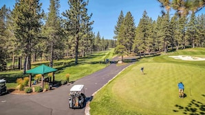 A golf course with a clear path, a covered seating area, and a person preparing to take a shot. - Tahoe Donner 4 bd Family Cabin (Truckee)