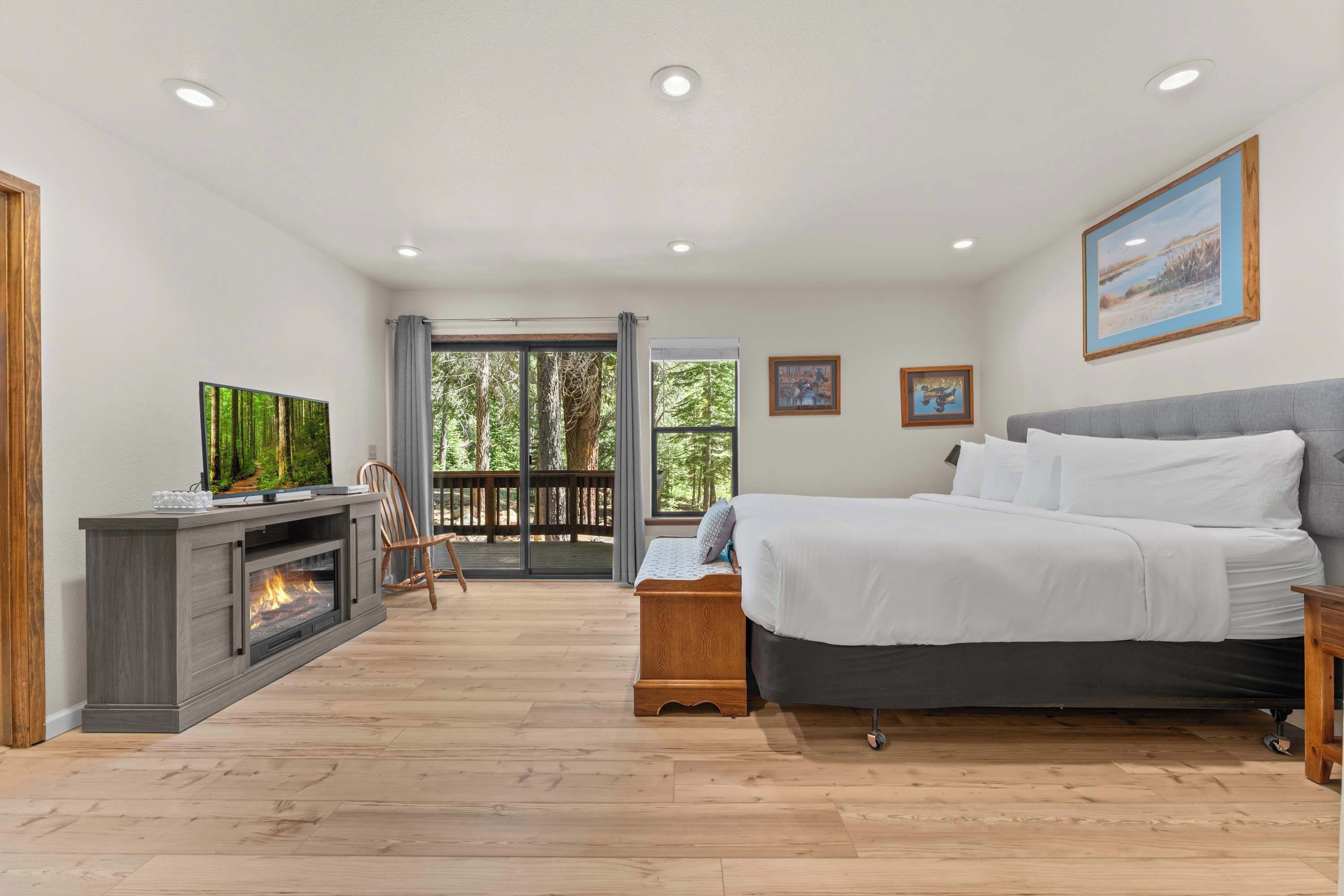 A bedroom with a bed, a TV, a fireplace, and a balcony with a view of trees.