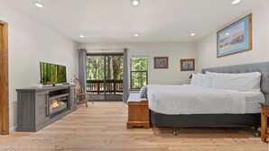 A bedroom with a bed, a TV, a fireplace, and a balcony with a view of trees. - Tahoe Donner 4 bd Family Cabin (Truckee)