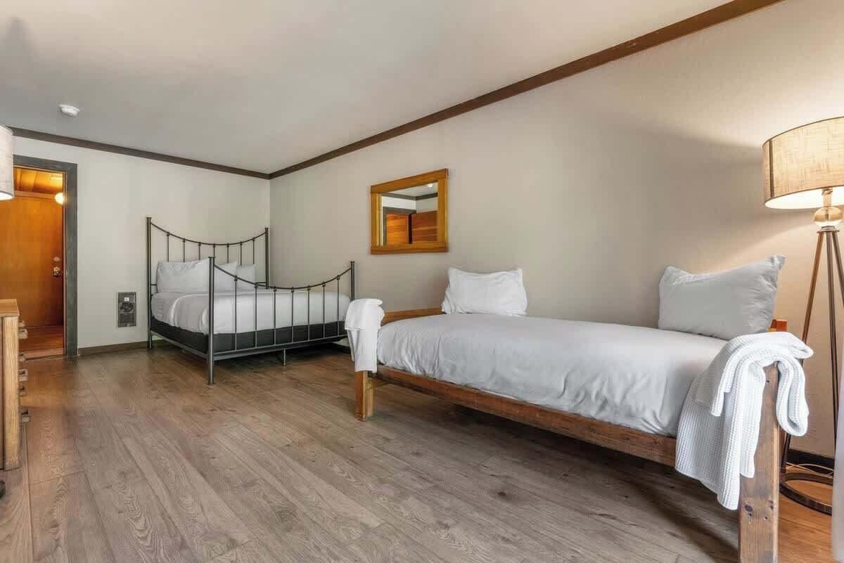 Quarto com cama, mesa de cabeceira, abajur e espelho na parede.