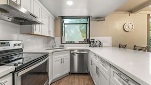 A modern kitchen with white cabinets, a stainless steel dishwasher, and a window providing natural light.