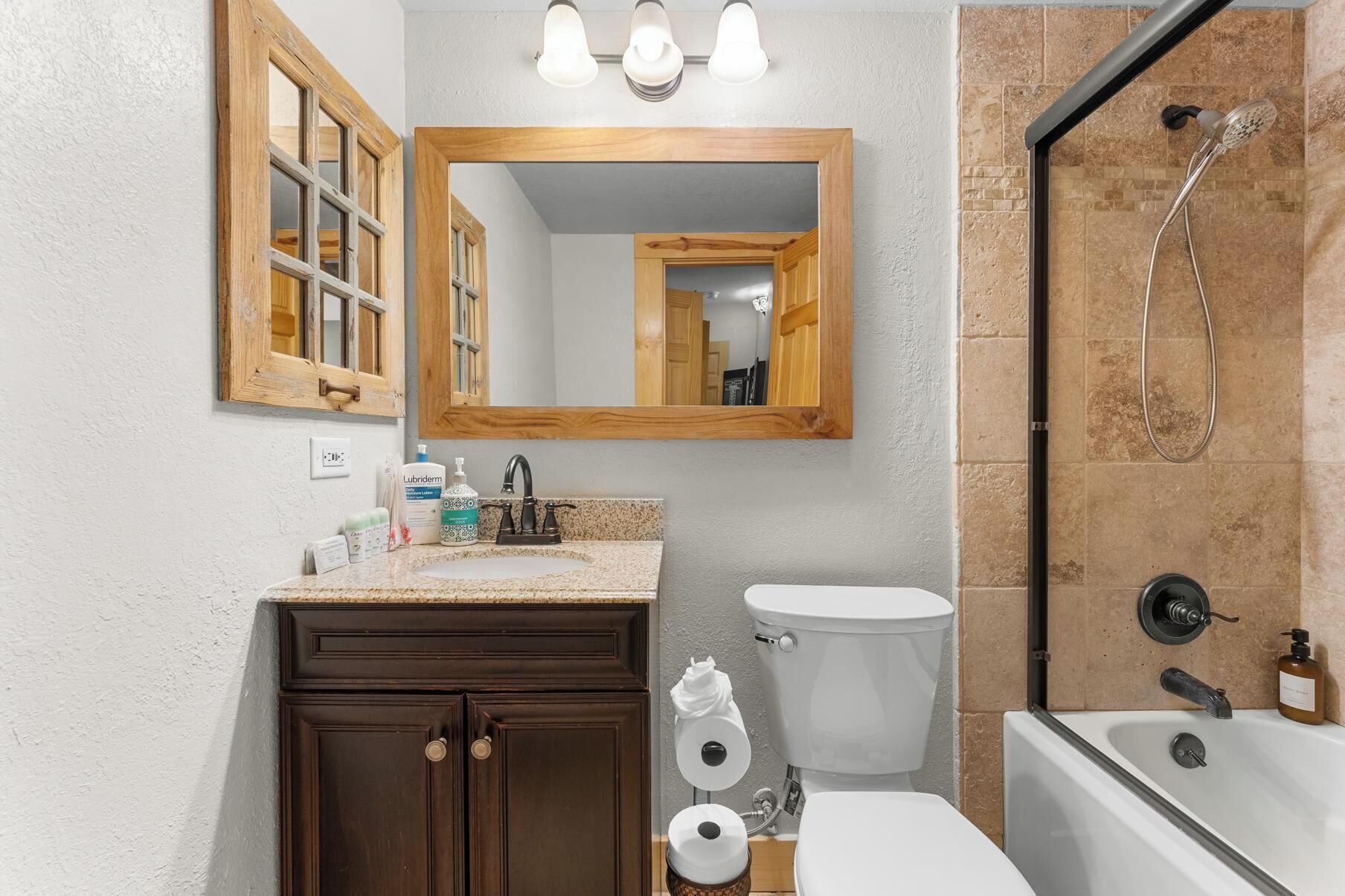 A bathroom with a wooden vanity, a large mirror, a toilet, a shower, and a sink.