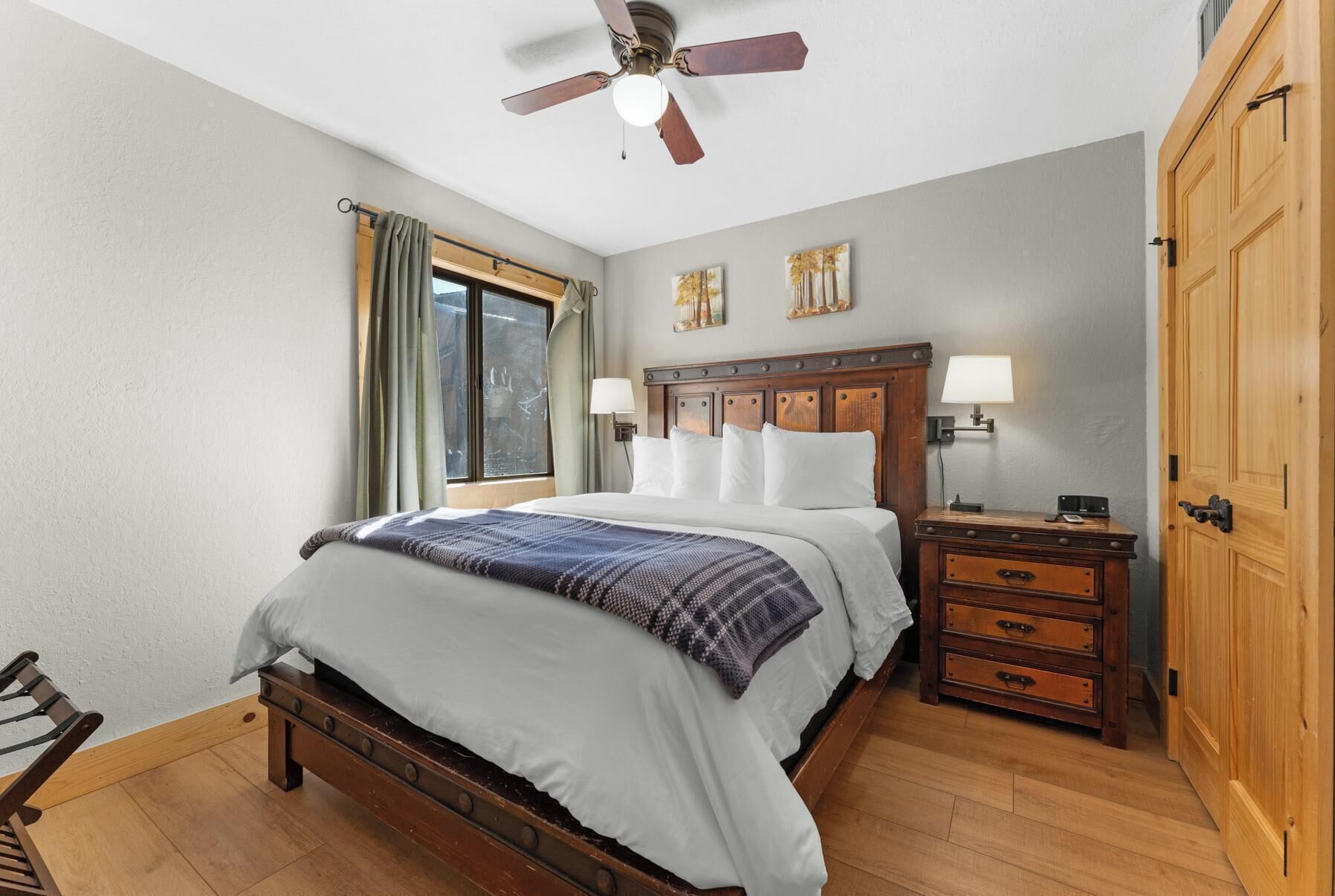 A bedroom with a wooden bed, a nightstand, a dresser, a ceiling fan, and a window with curtains.