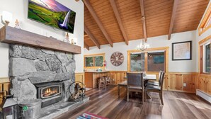 A cozy living room with a stone fireplace, wooden ceiling beams, and a television mounted on the wall. - Donner Lake Retreat Walk To Beach (Truckee)