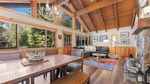 A spacious room with a wooden ceiling, large windows, a dining area, and a cozy seating area with a fireplace. - Donner Lake Retreat Walk To Beach (Truckee)