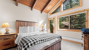 A bedroom with a wooden ceiling, a large window, a bed with a checkered bedspread, and two bedside lamps. - Donner Lake Retreat Walk To Beach (Truckee)