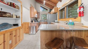 A modern kitchen with wooden cabinets, a stainless steel refrigerator, and a large island with bar stools. - Donner Lake Retreat Walk To Beach (Truckee)