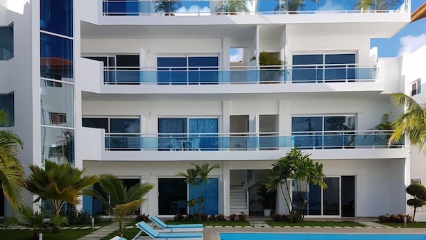Ein modernes, mehrstöckiges Hotel mit Pool, Liegestühlen und Palmen.