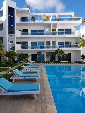 A modern multi-story hotel with a pool, sun loungers, and palm trees. - Baya Azul Bayahibe - Apto 306 (San Rafael del Yuma)