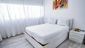 Ein modernes Schlafzimmer mit einem großen Bett, weißen Vorhängen und einem farbenfrohen abstrakten Gemälde an der Wand.