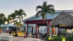 Een resort met een zwembad, een overdekt terras en een constructie met rieten dak.