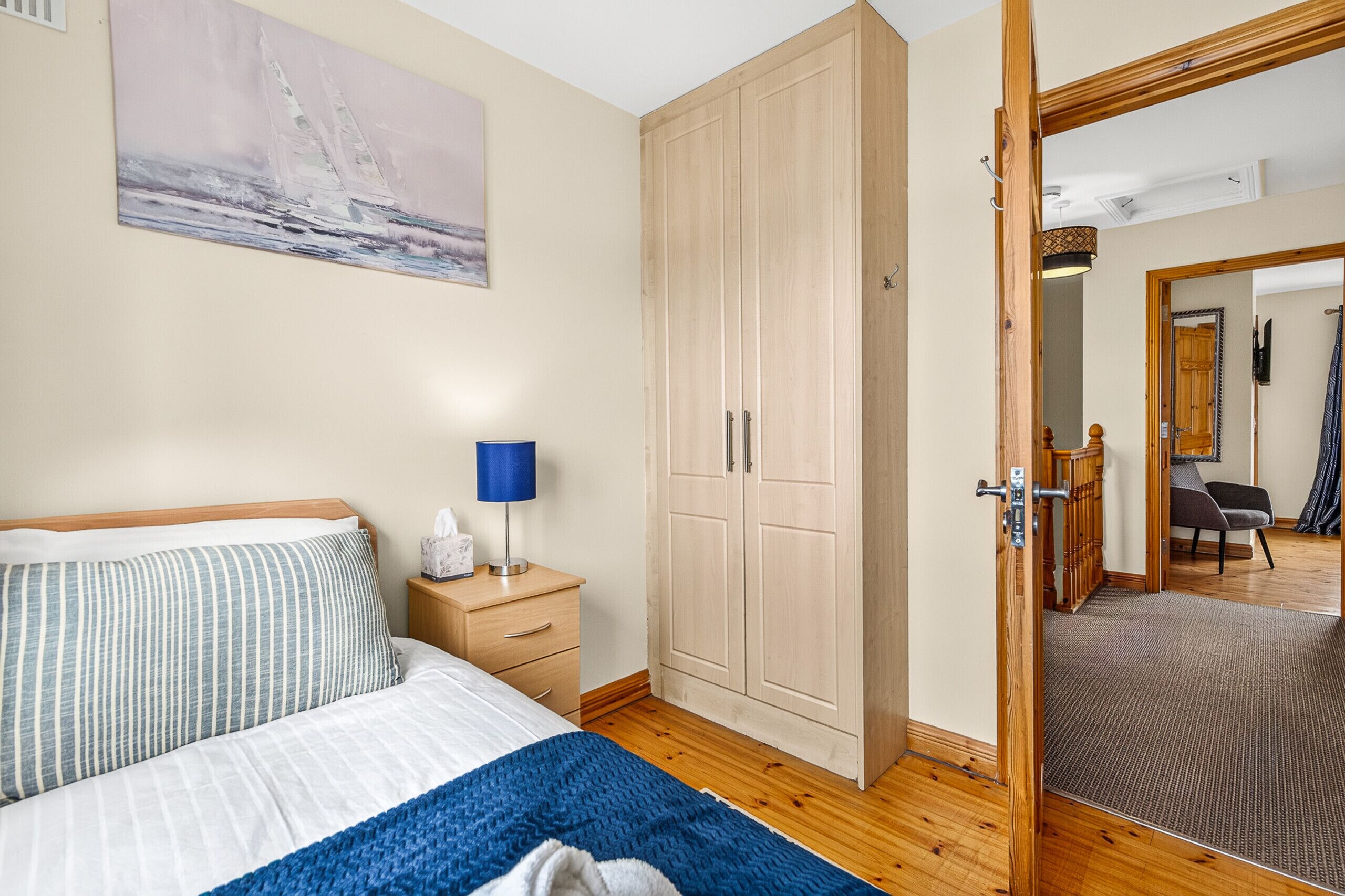 Une chambre à coucher comprenant un lit, une table de chevet, une lampe, une armoire et un miroir qui reflète une pièce avec une chaise et une porte.
