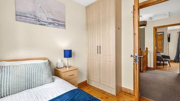 Une chambre à coucher comprenant un lit, une table de chevet, une lampe, une armoire et un miroir qui reflète une pièce avec une chaise et une porte.