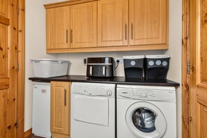 A compact kitchen with wooden cabinets, a washing machine, a dishwasher, and a coffee maker.