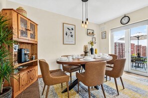 A dining area with a wooden table, brown chairs, a coffee machine, and a potted plant.