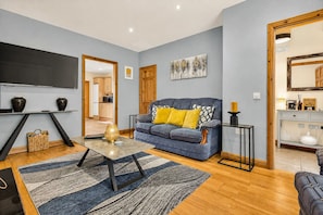 A living room with a sofa, a coffee table, a TV, and a kitchen in the background.