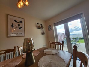 Un comedor con una mesa, sillas, una lámpara en el centro y vistas a un patio exterior por una puerta de vidrio.