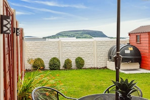 Un jardin avec un mur en pierre, un barbecue et une vue sur une colline.
