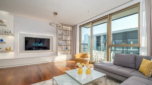 Ein modernes Wohnzimmer mit einem Flachbildfernseher, einer Couch, einem Couchtisch und einem großen Fenster mit Blick auf die Stadt.