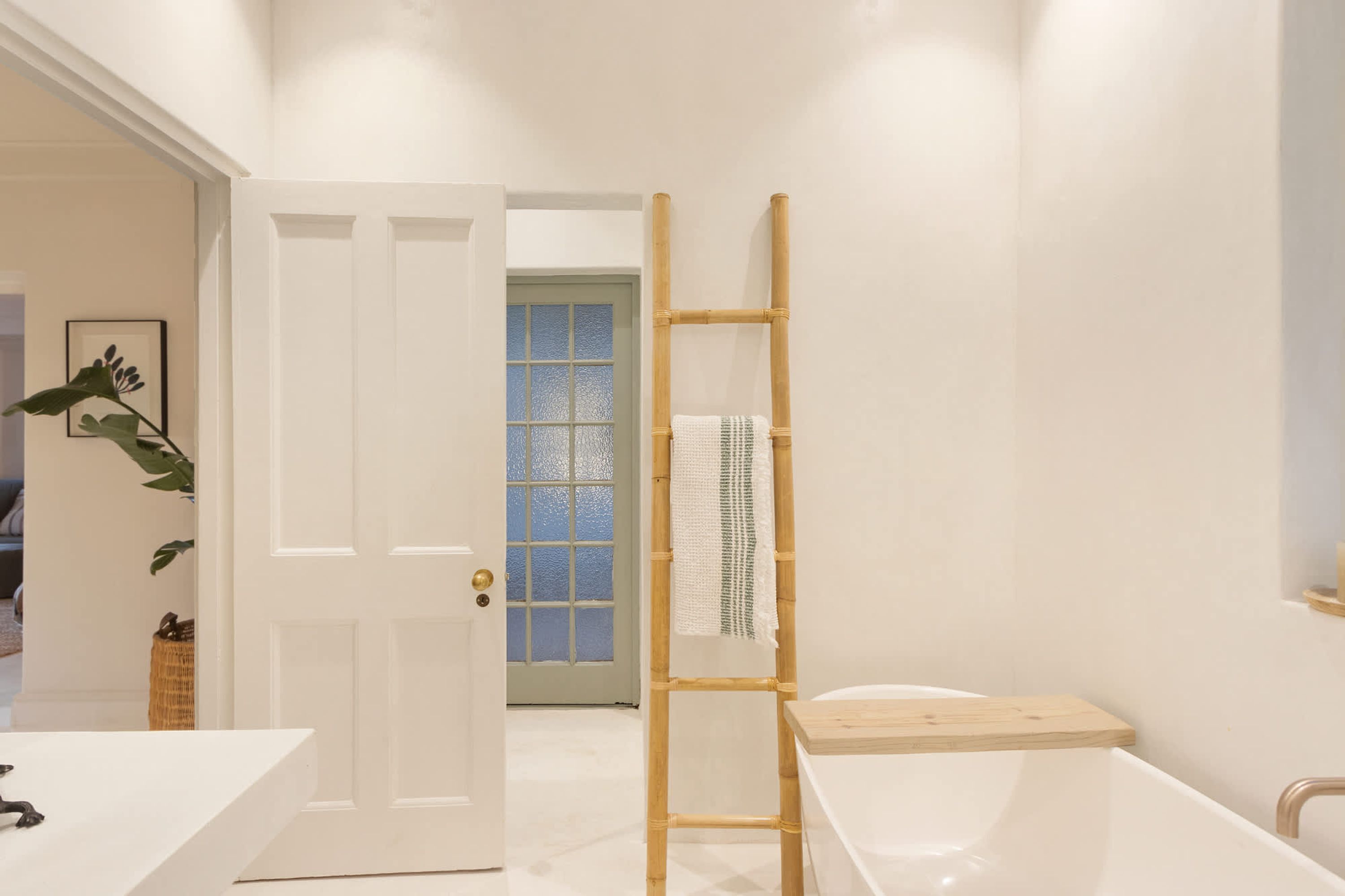 Ein Badezimmer mit einer weißen Badewanne, einer Holzleiter, einer weißen Tür und einem Fenster mit Milchglas.