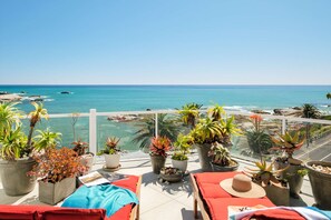 A terrace with red lounge chairs, potted plants, and a view of the sea.