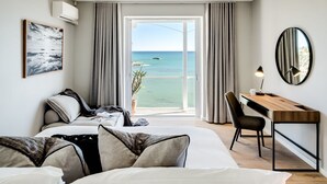 Une chambre d’hôtel équipée d’un lit, d’un bureau, d’une chaise, d’une grande fenêtre donnant sur la mer et d’un ventilateur de plafond.