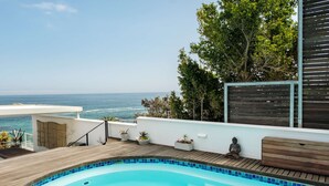 Une piscine avec vue sur l’océan, entourée d’une terrasse en bois et agrémentée de plantes en pot.
