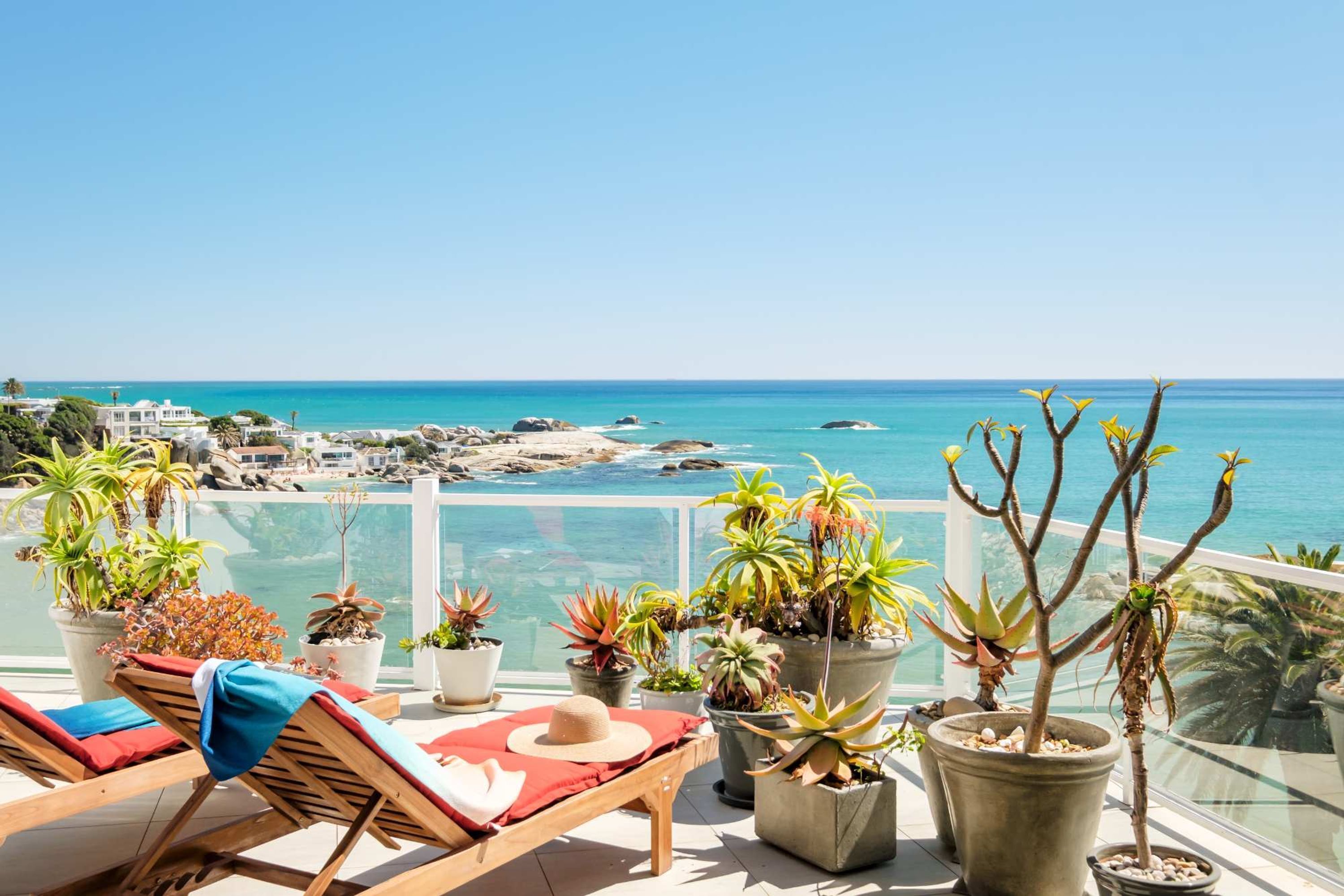 A balcony with lounge chairs, potted plants, and a view of the sea.